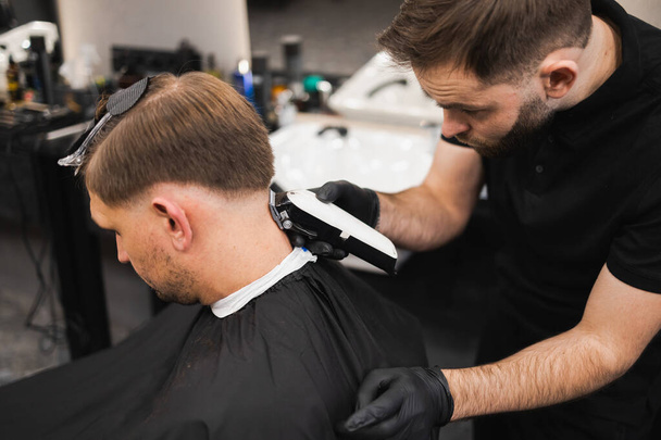 バーバーショップの若い男。美容師は電気クリッパーでクライアントの頭の後ろから髪をカットします - 写真・画像