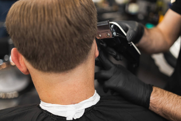 Close-up of a hairdresser cutting a client's hair with a electric clipper - Foto, afbeelding