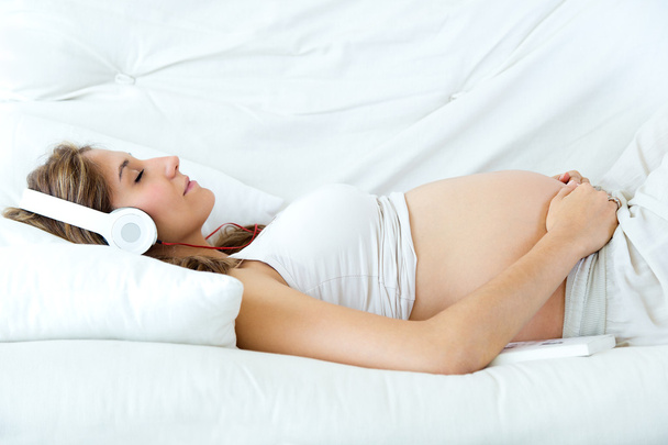 Pregnant woman sitting on sofa and listening music in headphones. - Fotografie, Obrázek