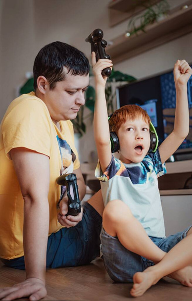 Время вместе отец и сын играют в видеоигры, ребенок рыжий мальчик выиграл. - Фото, изображение