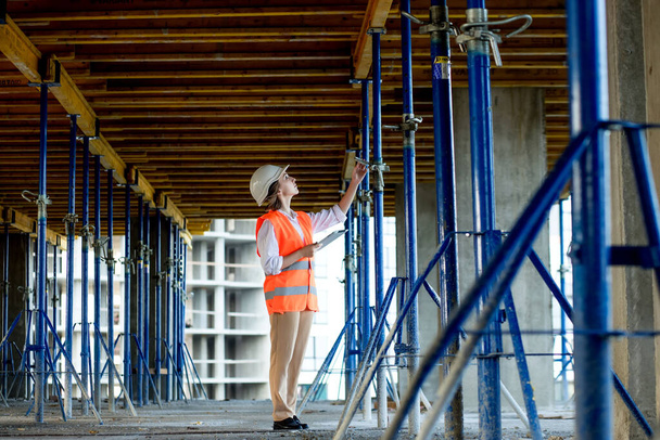 Confident Female builder checks fastenings on a monolithic structure. Construction concept. - Valokuva, kuva