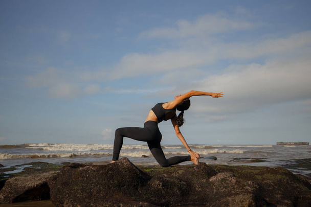 Πρωινή γιόγκα παραλίας. Ασιάτισσα που εξασκείται στην Ανζανγιασάνα. Χαμηλή Lunge. Κρέσεντ Μουν Πόουζ. Ιπποκράτισσα Πόζα. Γέρνω πίσω λυγίζοντας την Ασάνα. Ευέλικτο υγιές λεπτό σώμα. Yoga καταφύγιο. Mengening beach, Μπαλί - Φωτογραφία, εικόνα
