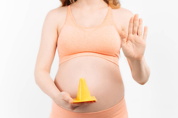 Pregnant woman and expecting a baby over isolated white background, holding her hands on her stomach and showing a prohibition sign. Warning expression with negative and serious gesture - Φωτογραφία, εικόνα