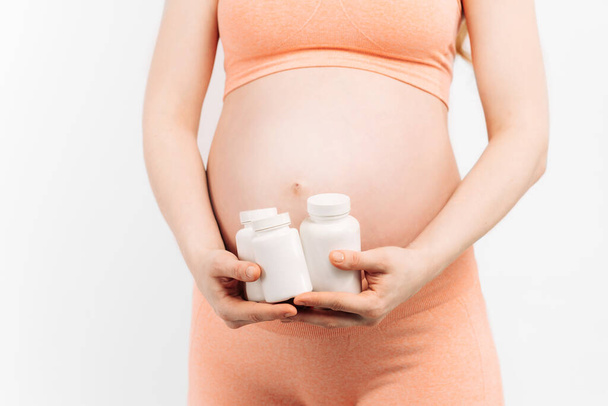 Close-up of a pregnant belly with medicine on a white background. A woman is expecting a baby, with pills. Taking medication or vitamins during pregnancy - Foto, imagen