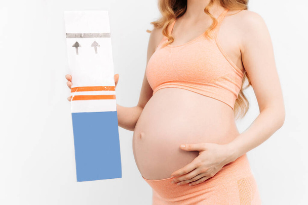 Pregnant woman holding a positive pregnancy test in her hands on a white background. Happy woman with pregnancy test. Waiting for a child. Concept of love, happiness and security - Foto, immagini