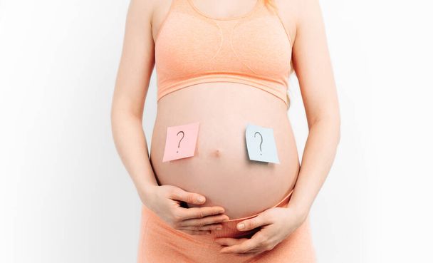 pregnant woman holding a paper with a question mark wondering about the gender of the baby. Expectant mother thinks about a newborn baby. Motherhood and upbringing. Planned pregnancy and IVF. - 写真・画像