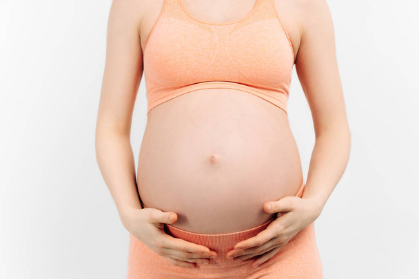pregnant woman holds her hands on her stomach on a white background. Pregnancy, motherhood, preparation and expectation concept. Close-up, Beautiful tender mood photo of pregnancy. - Φωτογραφία, εικόνα