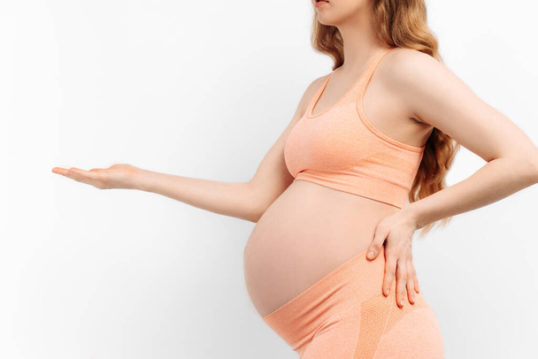 pregnant woman holds her hands on her stomach on a white background. Pregnancy, motherhood, preparation and expectation concept. Close-up, Beautiful tender mood photo of pregnancy. - Foto, Bild