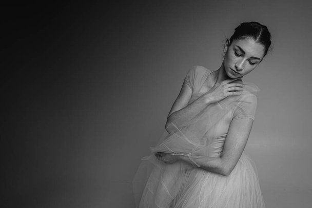 Fekete-fehér fotó, közeli kép egy balerináról. Fiatal elegáns balett táncos, öltözött professzionális ruhák, érzelmi, visszafogott, szelektív fókusz. A klasszikus balett szépsége - Fotó, kép