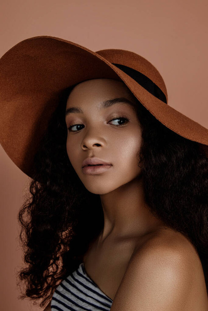 Beauty portrait of sensual young female in hat. Clean skin. Healthy care. Portrait of beautiful african american in hat isolated. Studio shoot. Portrait of beauty model with natural nude make up - Fotó, kép