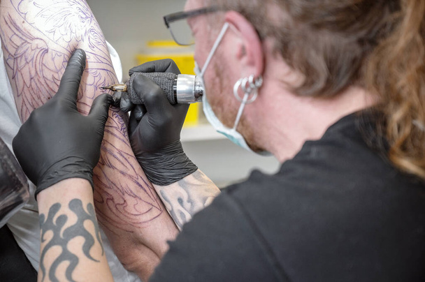 Τατουάζ σαλονιού. Κοντινό πλάνο ενός καλλιτέχνη τατουάζ που εργάζεται. Καλλιτέχνης τατουάζ κάνει τατουάζ στο στούντιο. - Φωτογραφία, εικόνα