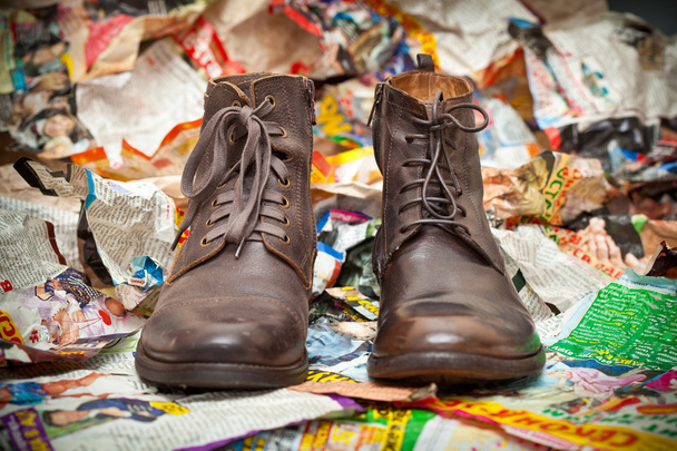 Men's leather boots standing next to crumpled scraps of paper - grunge style. Prestige autumn - spring shoes - Photo, Image