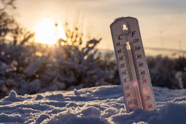 Das Thermometer zeigt auf Schnee niedrige Temperaturen in Grad Celsius oder Farenheit an. Auf dem Sonnenuntergang. - Foto, Bild