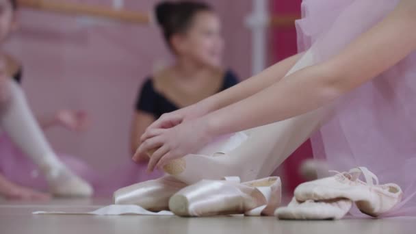 Entrenamiento de ballet: chicas con hermosos vestidos sentadas en el suelo y una de ellas poniéndose zapatos puntiagudos - Imágenes, Vídeo