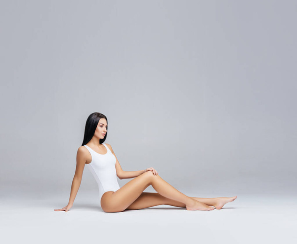 Attractive and slender brunette girl in white underwear posing in studio. Healthy lifestyle, sport and body care concept. - Fotó, kép