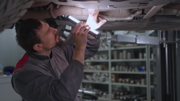Ein Vorarbeiter inspiziert die Auspuffanlage eines Autos - Filmmaterial, Video