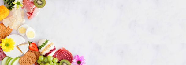 Spring or Easter charcuterie corner border against a white marble banner background. Top down view. Assortment of cheese, meat and fruit appetizers. Copy space. - 写真・画像