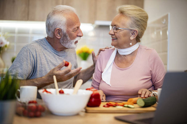 Старша пара готує здорову їжу. Старша пара розмовляє і посміхається, готуючи здорову їжу на термальній кухні. Концепція блогів
. - Фото, зображення