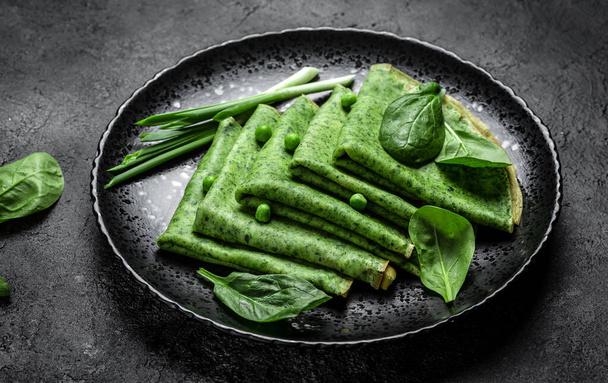 Green vegan crepes with spinach on dark background. Healthy breakfast, vegetarian food, banner, menu recipe place for text, top view. - Photo, Image