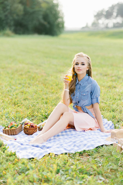 Портрет молодой женщины, держащей апельсиновый сок в стакане в открытом парке. - Фото, изображение