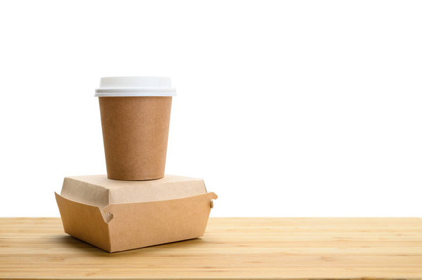Papierowy kubek na kawę i pojemnik z hamburgerem na drewnianym stole na białym, izolowanym tle. przestrzeń kopiowania. - Zdjęcie, obraz