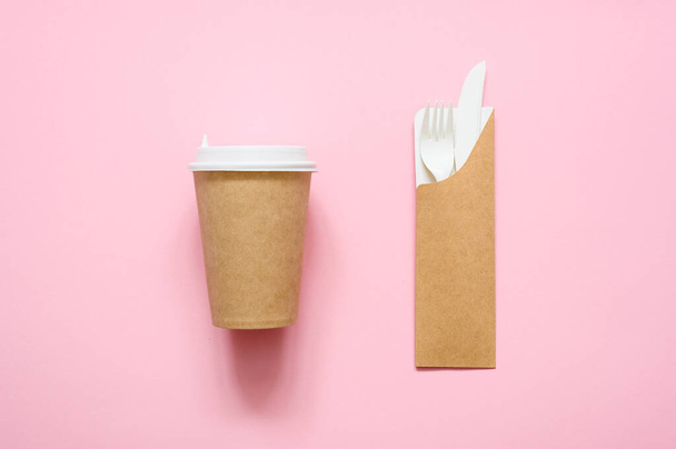 Taza de papel para café y tenedor desechable con un cuchillo en una caja de cartón sobre un fondo rosa - Foto, Imagen