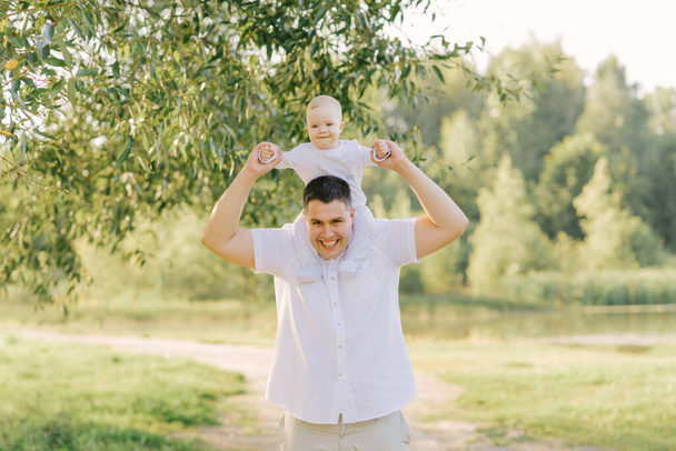 Młody szczęśliwy ojciec dużych rozmiarów trzyma swojego synka na szyi w parku latem - Zdjęcie, obraz