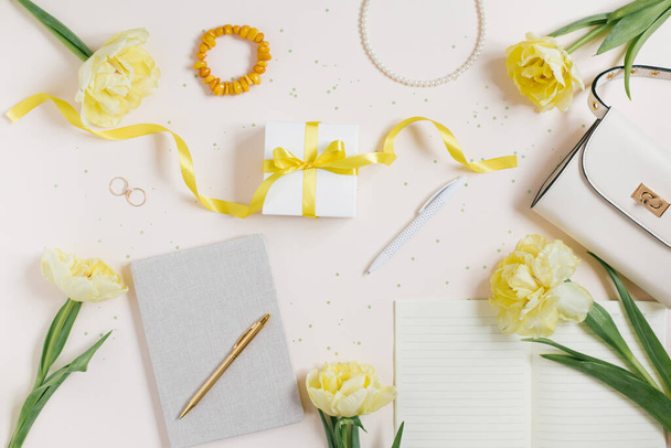 Arbeitsplatz mit Notizbuch und Stift, gelben Tulpen, einem Armband, einer Damenhandtasche auf hellem Hintergrund. Flache Zusammensetzung für Blogger, Magazine, soziale Medien und Künstler. Ansicht von oben - Foto, Bild