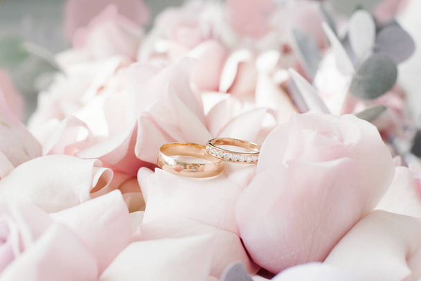 Gold wedding rings lie on delicate pink roses close-up - Fotoğraf, Görsel