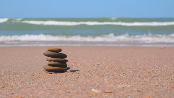 De zeegolf rolt over de zandkust. Een stapel kiezelstenen zijn gestapeld in een piramide. Zen meditatie, harmonie, balans - Video