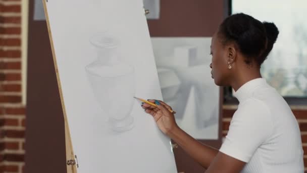 アフリカ系アメリカ人女性が白いキャンバスに花瓶モデルを描く - 映像、動画