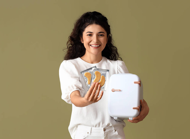 Junge Frau mit kosmetischem Kühlschrank und Augenklappen auf farbigem Hintergrund - Foto, Bild
