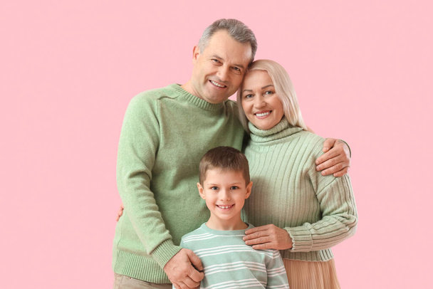 Petit garçon avec ses grands-parents dans des pulls chauds étreignant sur fond rose - Photo, image