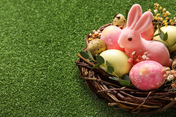 Nido con uova di Pasqua dipinte, coniglietto e fiori su sfondo verde, primo piano - Foto, immagini