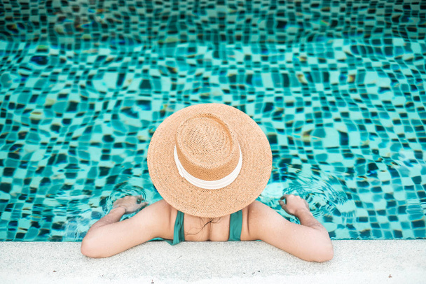 Boldog nő zöld fürdőruhában és sapkában úszómedencében egy luxushotelben az óceán partja ellen. fiatal nők élvezik a trópusi üdülőhelyet. Pihenés, nyár, utazás, nyaralás, nyaralás és hétvége koncepció - Fotó, kép