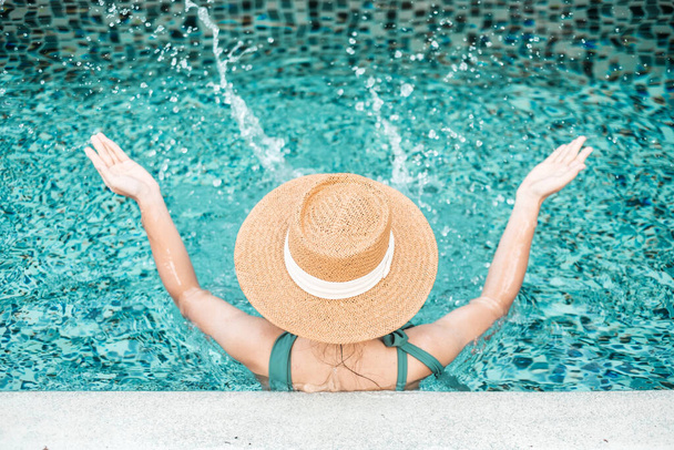 緑の水着で幸せな女性と海の正面に対して豪華なホテルでスイミングプールで帽子。若い女性は熱帯リゾートでお楽しみください。リラックス、夏、旅行、休日、休暇、週末のコンセプト - 写真・画像