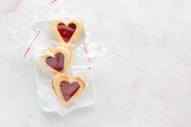 Cellophane bags with heart shape Linzer cookies inside, on a white plate - Fotografie, Obrázek