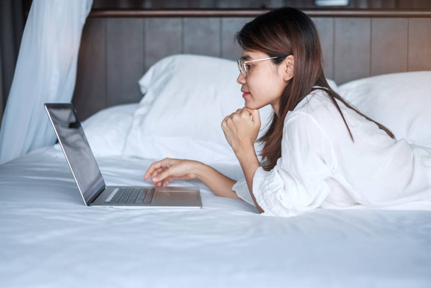 Szczęśliwa kobieta korzystająca z laptopa do pracy, spotkanie kobiet online przez notatnik komputerowy na łóżku. technologia, sieć, praca w domu, koncepcja stylu życia i komunikacji cyfrowej - Zdjęcie, obraz