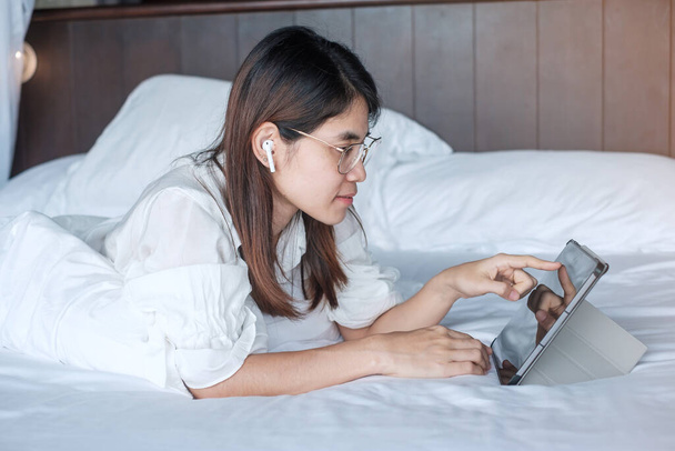 Mujer feliz usando la tableta para las redes sociales, joven mujer viendo películas en la almohadilla de la computadora en la cama en casa. tecnología, red, compras en línea, comercio electrónico, estilo de vida y concepto de comunicación digital - Foto, imagen