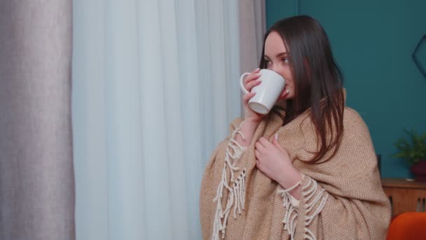Chica morena adulta joven en suéter blanco cálido beber taza de bebida caliente relajarse en casa cerca de la ventana - Imágenes, Vídeo