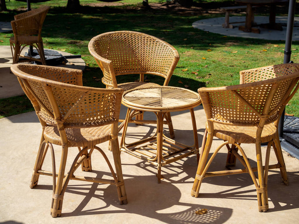 Puste meble rattanowe, stolik splot ogrodowy z okrągłym stołem i trzy krzesła na zielonej betonowej podłodze w zielonym podwórku, prosta konstrukcja. - Zdjęcie, obraz