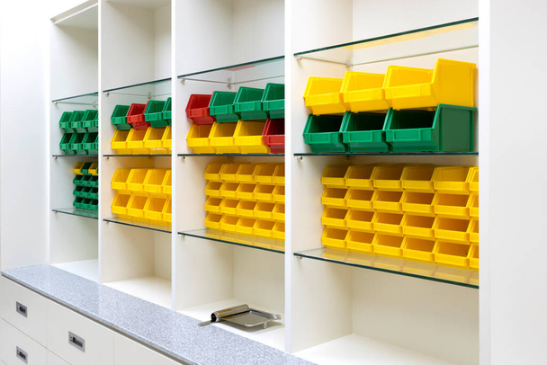 Fényesen színezett műanyag tálcák sora modern stílusú tárolópolcokon. - Fotó, kép