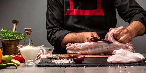 Шеф-повар режет тушу кролика сырым мясом, используя мясной тесак, руки шеф-повара готовят кролика. Длинный формат баннера, - Фото, изображение
