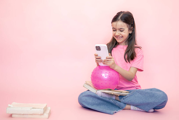 Маленька дівчинка зі смартфоном в руках на рожевому тлі, копіювати простір
. - Фото, зображення