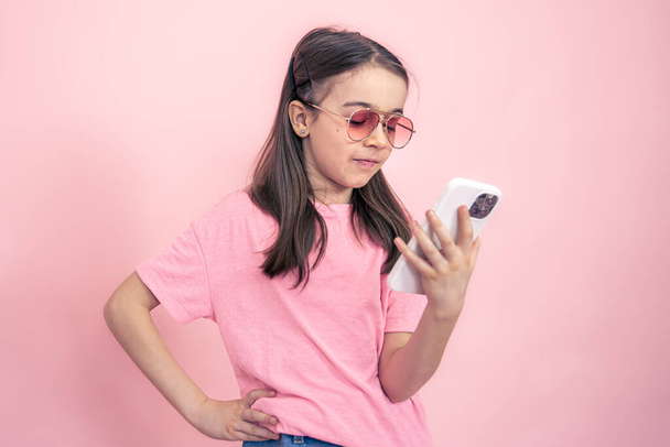 Stylish little girl with a smartphone on a pink background. - Zdjęcie, obraz