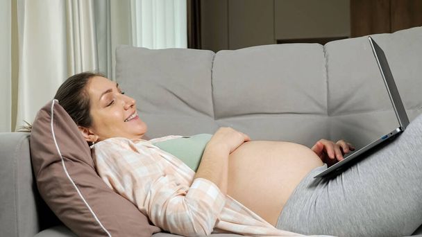 Zwangere moeder doet online winkelen voor baby liggend op de bank - Foto, afbeelding