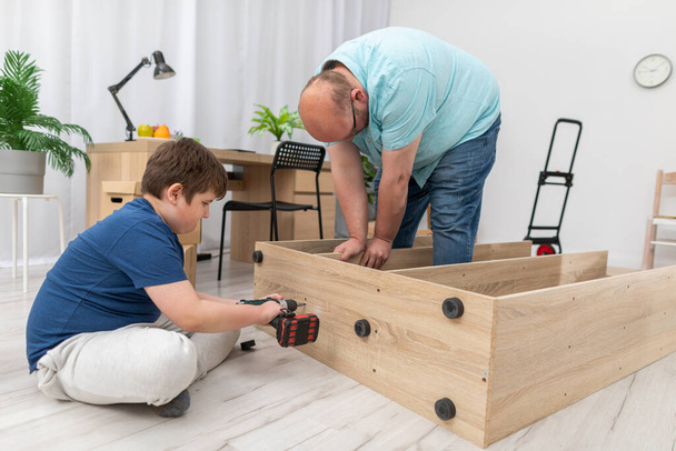 The son screws the screws with a screwdriver and the father holds the bookcase. - Photo, Image