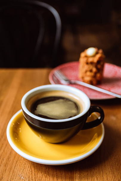 Ένα κεραμικό φλιτζάνι μαύρο καφέ και ένα επιδόρπιο σερβίρεται σε ένα πιάτο στο ξύλινο τραπέζι σε ένα καφέ, ένα κοντινό πλάνο - Φωτογραφία, εικόνα