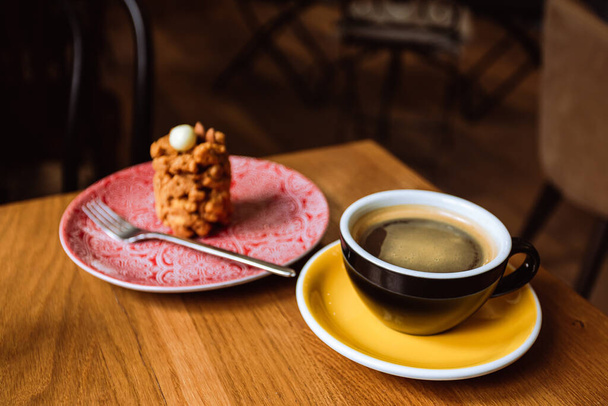 A ceramic cup of black coffee and a dessert served on a plate on the wooden table in a cafe. - Fotografie, Obrázek