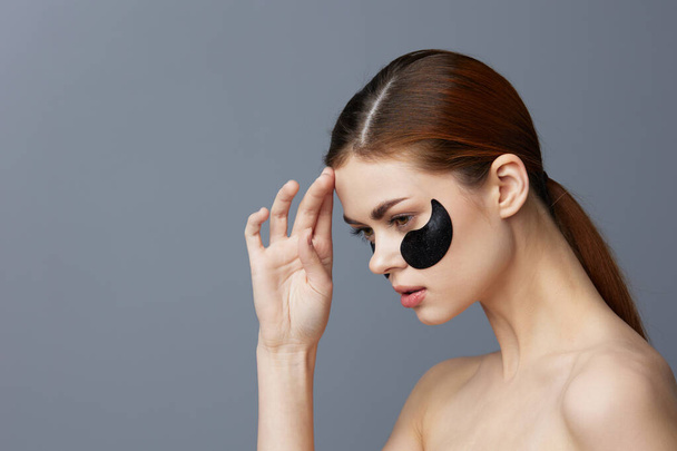 jonge vrouw ooglapjes op gezicht blote schouders huidverzorging geïsoleerde achtergrond - Foto, afbeelding